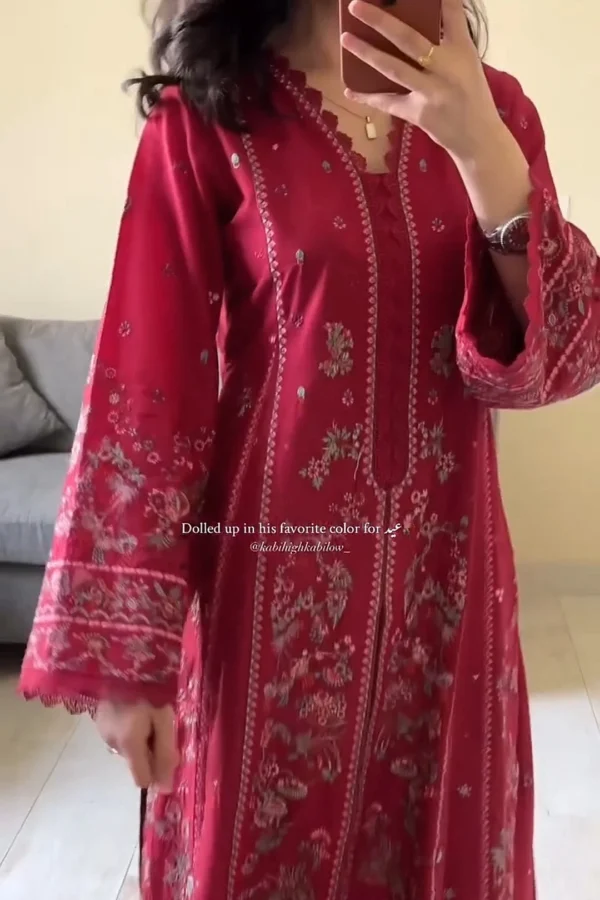 Woman wearing a deep red traditional embroidered kameez with floral and vine motifs in silver and light gold threads. The neckline features a scalloped lace design, and the long sleeves have intricate embroidery near the cuffs. She holds her phone in one hand, revealing a gold ring and a watch on the other wrist. Text on the image reads: "Dolled up in his favorite color for Eid." Let me know if you'd like a combined caption or product-style description for all three images.