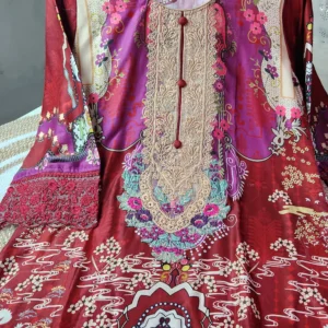 A vibrant traditional South Asian kurti in deep red and magenta tones with elaborate multicolor patterns and embroidery. The neckline features beige and gold lace embroidery accented with turquoise, pink, and purple floral threadwork, along with decorative red buttons down the center. The kurti showcases printed motifs of flowers, waves, and ornamental designs in cream, white, and various bright shades. The sleeves are adorned with intricate red lace embroidery. The garment is displayed on a black hanger against a neutral background.